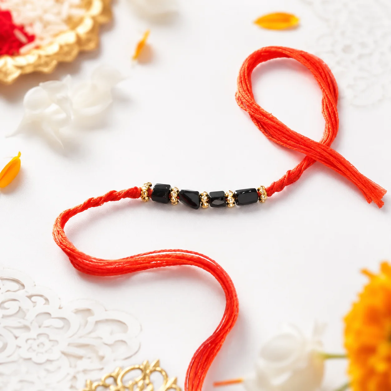 A minimalist rakhi featuring black semi precious stones and golden beads on a bright red thread, symbolizing strength and protection.